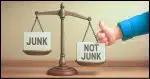 a balance scale with one side labeled "Junk", the other labeled "Not Junk" and an arm coming in from off camera putting a thumb on the Not Junk side to make it lower